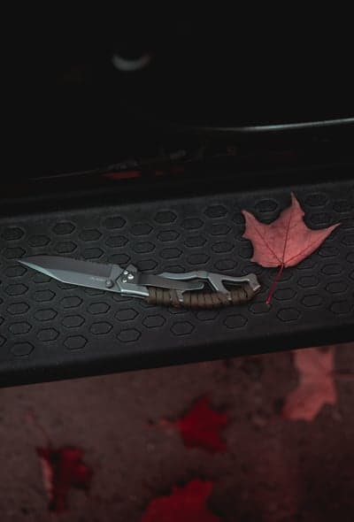 Tactical knife and fallen leaf on textured surface