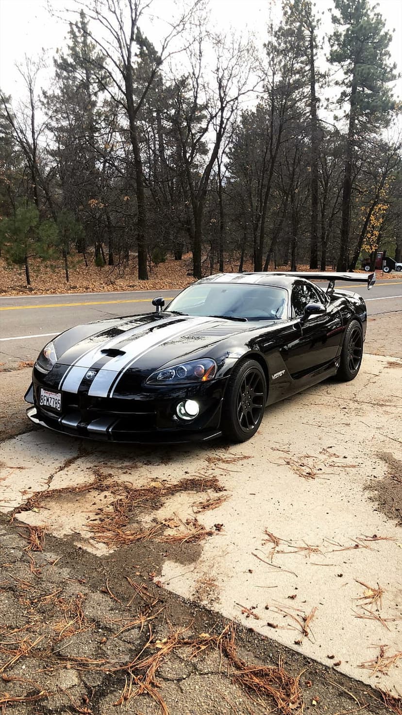 Black Dodge Viper SRT-10 ACR with white stripes and a large rear wing parked on a concrete roadside pad.