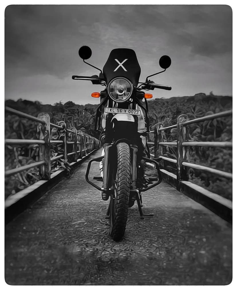 Motorcycle with an X mark on its windshield parked on a bridge surrounded by dark trees in grayscale.