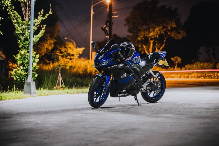Blue Yamaha sportbike with a black helmet on the seat parked on a dark street under glowing urban light streaks.