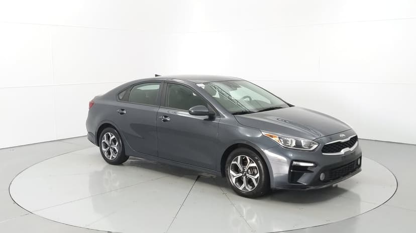 Dark grey Kia Forte sedan on a reflective white turntable in a minimalist automotive studio setting.