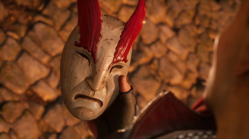 Weathered white mask with sharp red horns held by a gloved hand against a blurred warm-toned stone wall background.