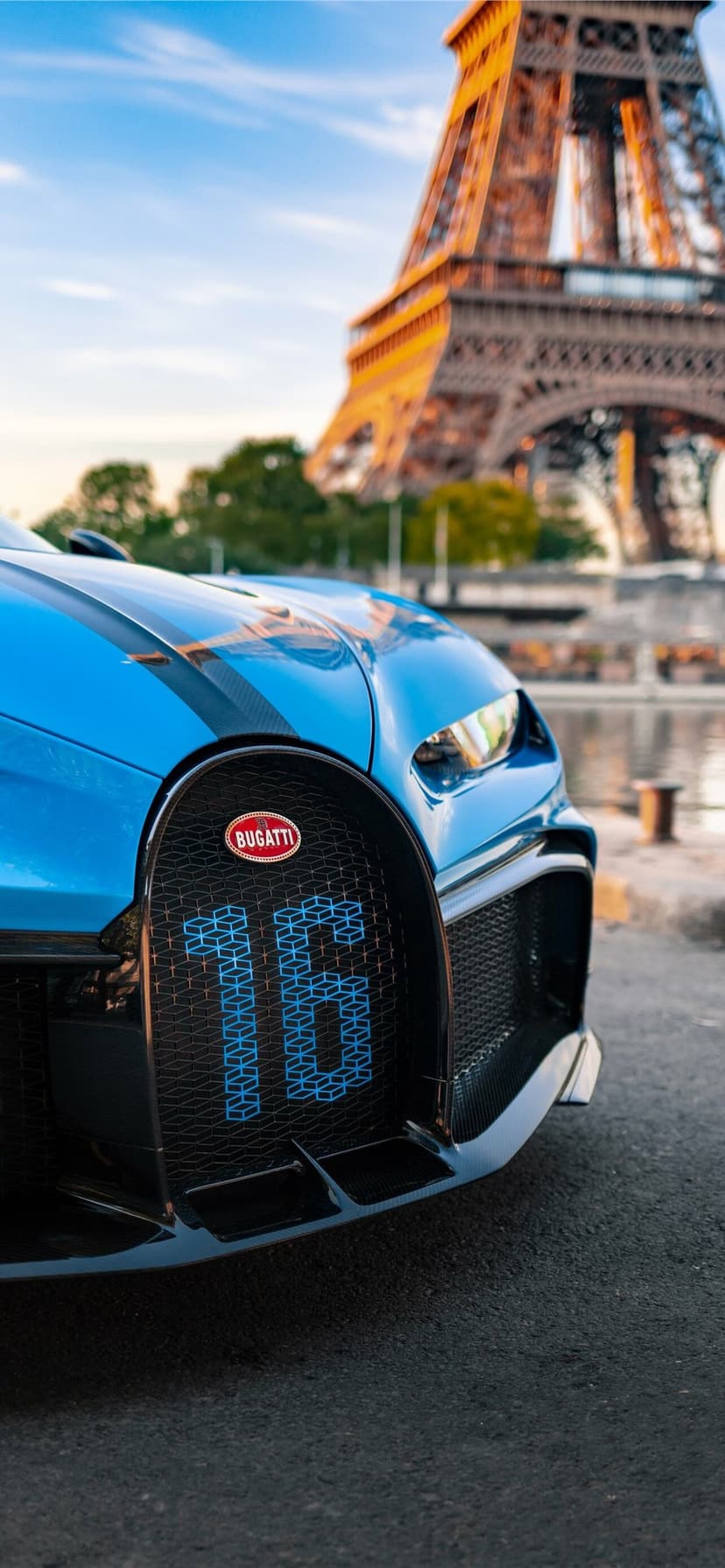 Close up of a blue Bugatti supercar grille with the number 16 and the Eiffel Tower blurred in the background.