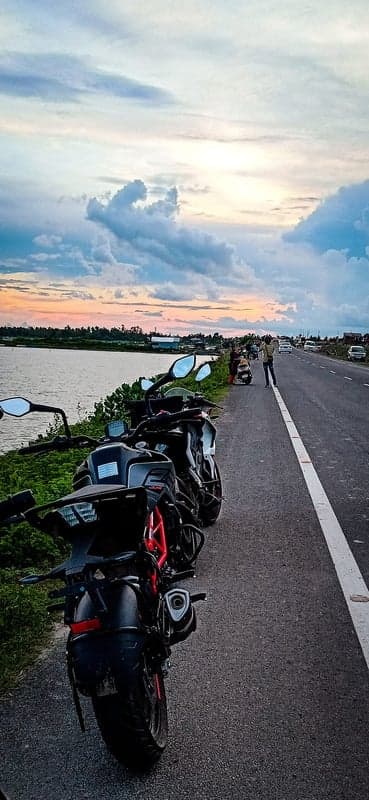Motorcycles by a river at sunset with cloudy sky