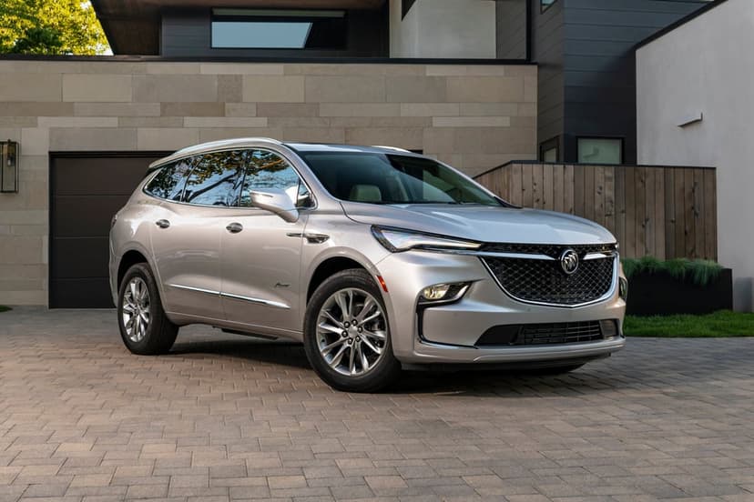 Silver Buick Enclave Avenir parked on a stone driveway in front of a modern house with wood and stone accents.