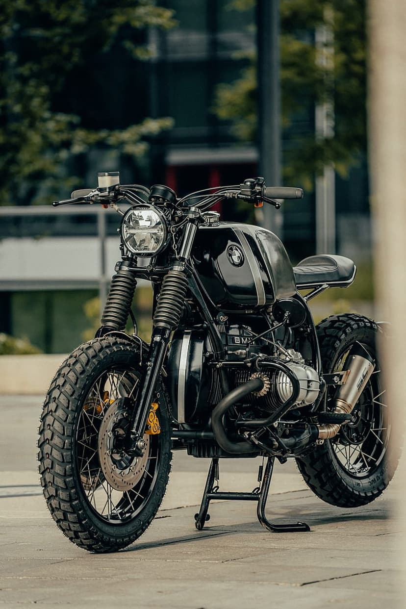 Black BMW R nineT Scrambler motorcycle with a round LED headlight and knobby tires in a blurred urban environment.