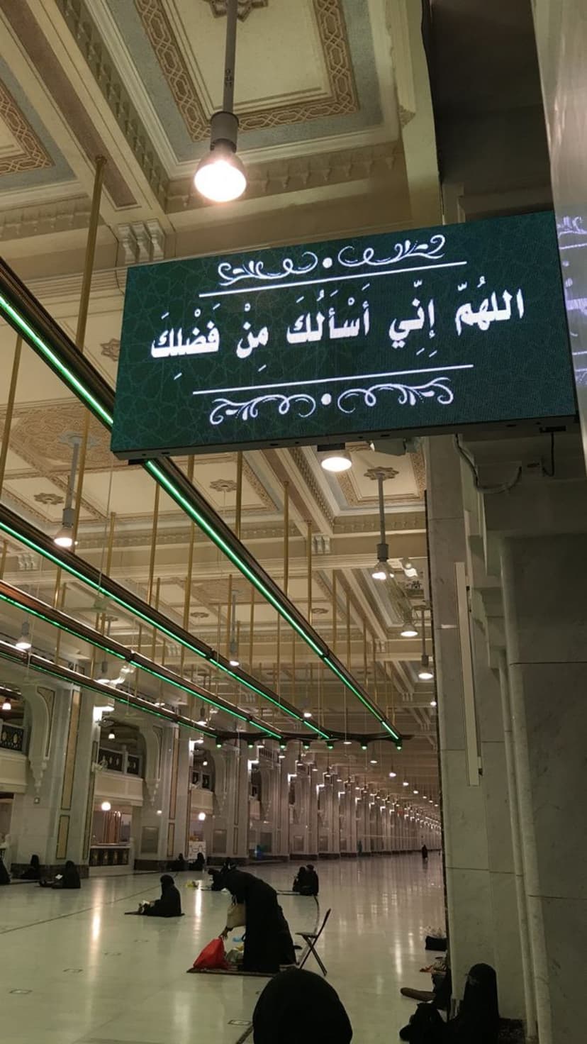Arabic Dua displayed on a green digital screen within the marble halls of Masjid Al Haram during prayer time.