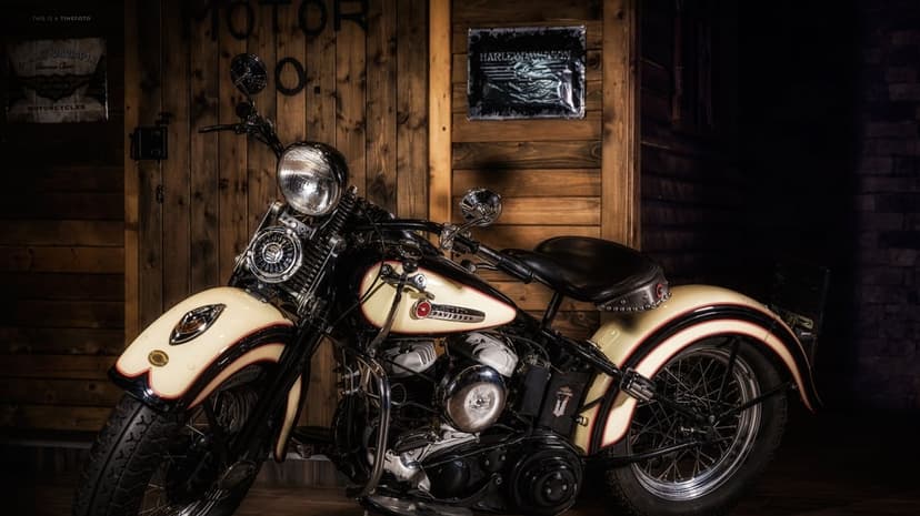 Classic cream and black Harley-Davidson motorcycle in a rustic wooden garage with moody lighting.