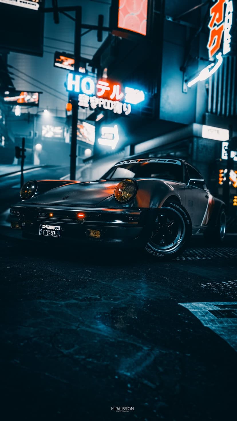 Classic Porsche with amber headlights in a dark Tokyo alleyway illuminated by red and blue neon Japanese signs.