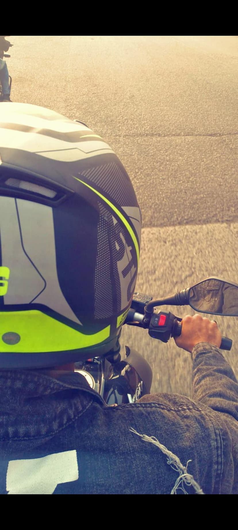Biker wearing a neon yellow helmet and denim jacket cruises on a sunlit road with hands on handlebars.