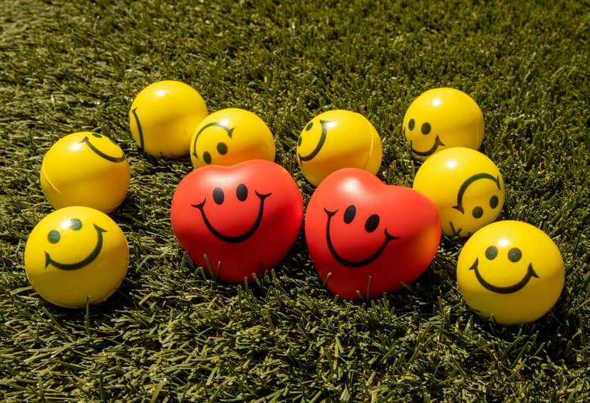 Yellow smiley face balls and red heart shapes scattered across lush green grass in a close-up outdoor scene.