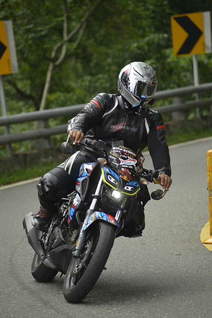 Motorcyclist in black leathers and silver helmet leaning a sportbike through a sharp asphalt road curve.