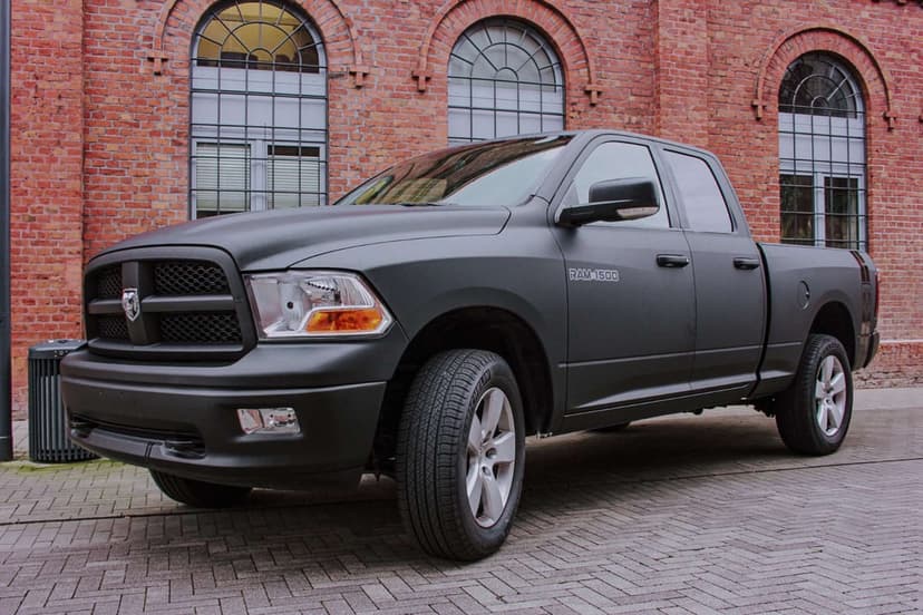 Matte black RAM 1500 truck parked on a cobblestone street in front of a red brick building.
