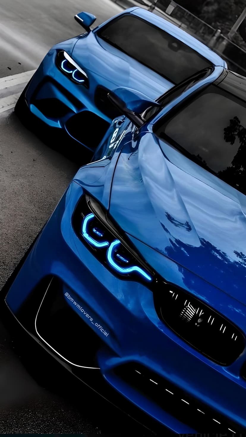 Two blue BMW sports cars with illuminated LED headlights parked on a city street at night under urban lights.