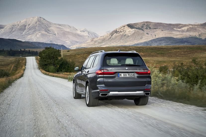 Dark gray BMW X7 SUV driving on a white gravel road with large mountains and hills in the background.