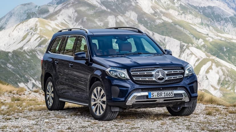A dark blue Mercedes-Benz GLS parked on a rocky ridge with massive, light-gray mountains in the background.