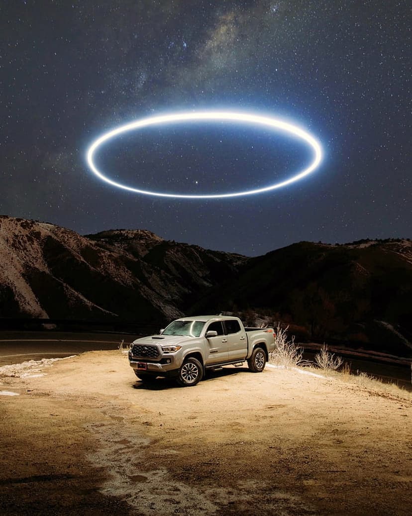Silver Toyota Tacoma truck parked in a dark desert under a glowing halo ring and the starry Milky Way galaxy sky.