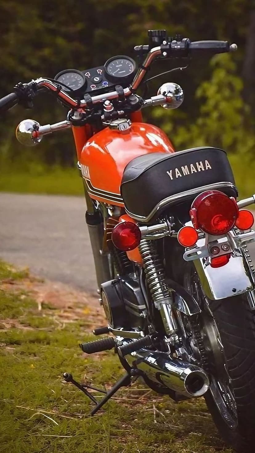 Orange Yamaha motorcycle rear view featuring chrome fenders and red taillights while parked on a grassy field.