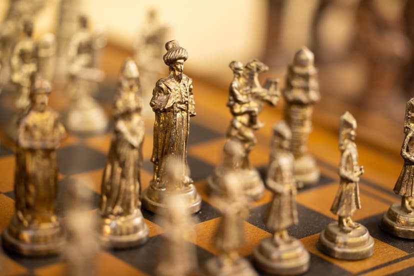 Golden king and queen chess pieces stand on a dark wooden board with warm lighting and shallow depth of field.
