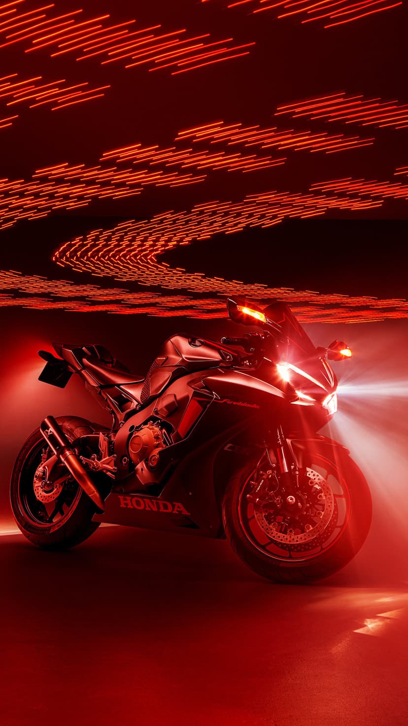 Honda CBR motorcycle illuminated by glowing red neon streaks and bright headlights against a dark night backdrop.