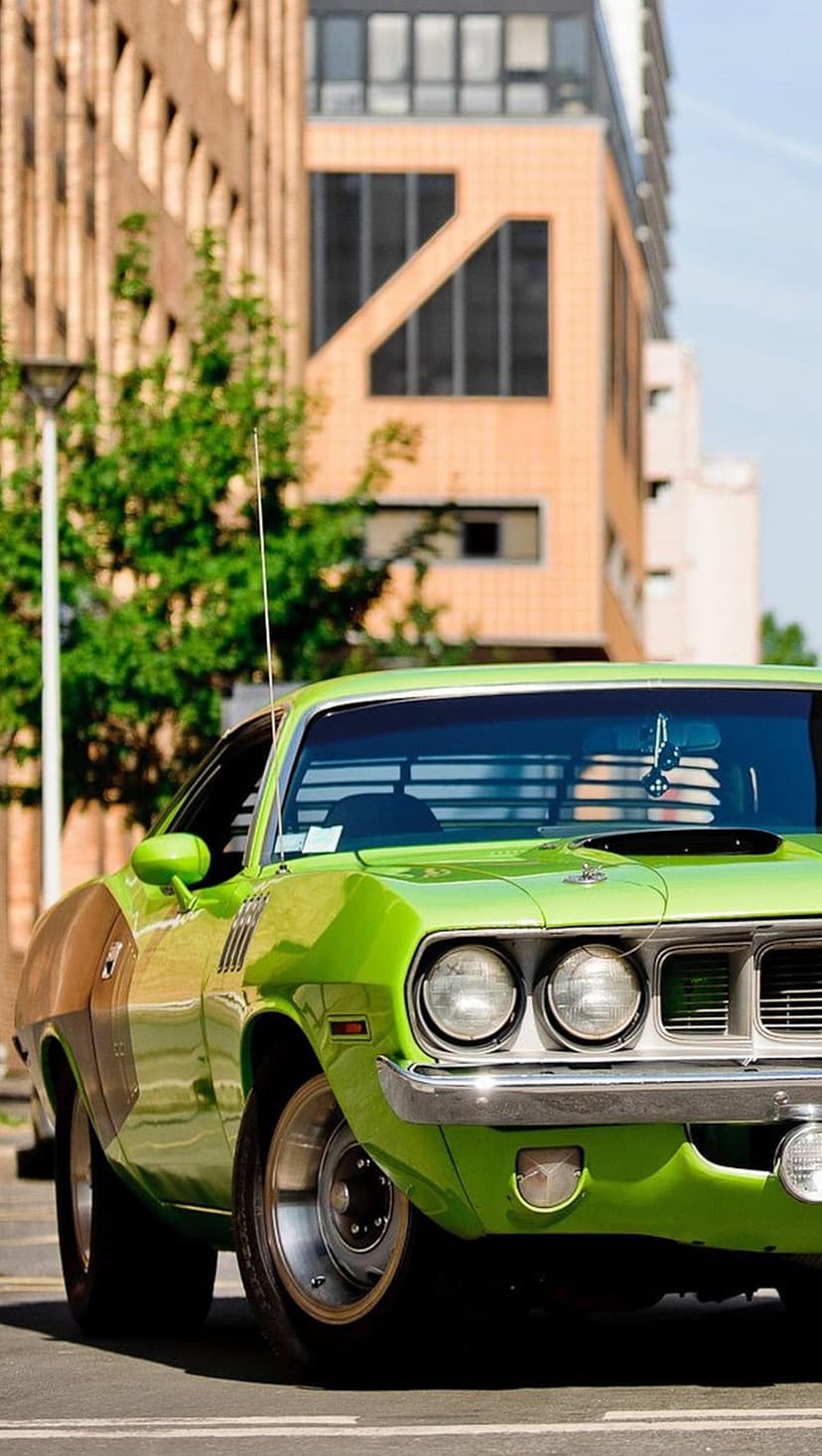 Lime green muscle car with a chrome grille and round headlights parked near an urban building with green trees.