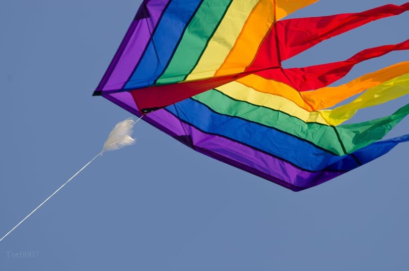 Rainbow kite with a long tail soaring through a clear blue sky during a bright, sunny afternoon outdoors.