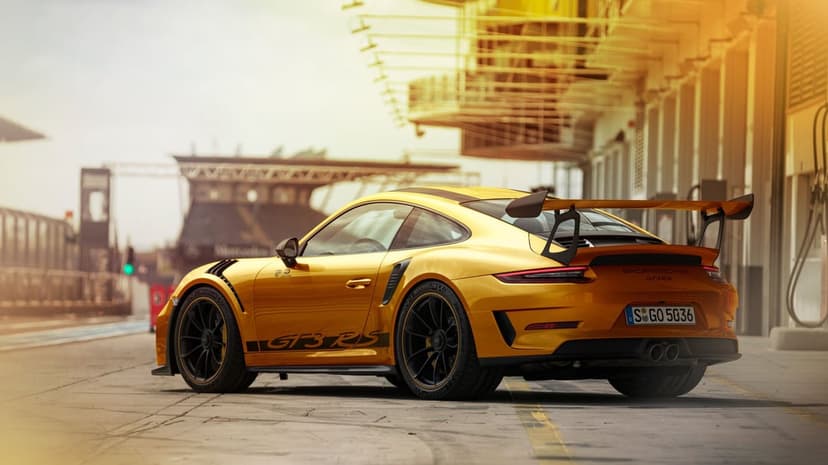 Rear view of a yellow Porsche 911 GT3 RS on a sunlit racetrack pit lane with a large rear wing.