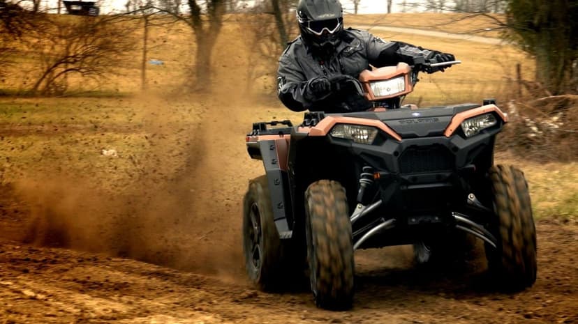 Rider on a copper Polaris ATV kicking up a massive dust cloud while turning on a dirt track in a field.