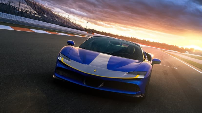 Blue Ferrari SF90 with silver stripe on a race track under a vibrant orange and purple sunset sky.