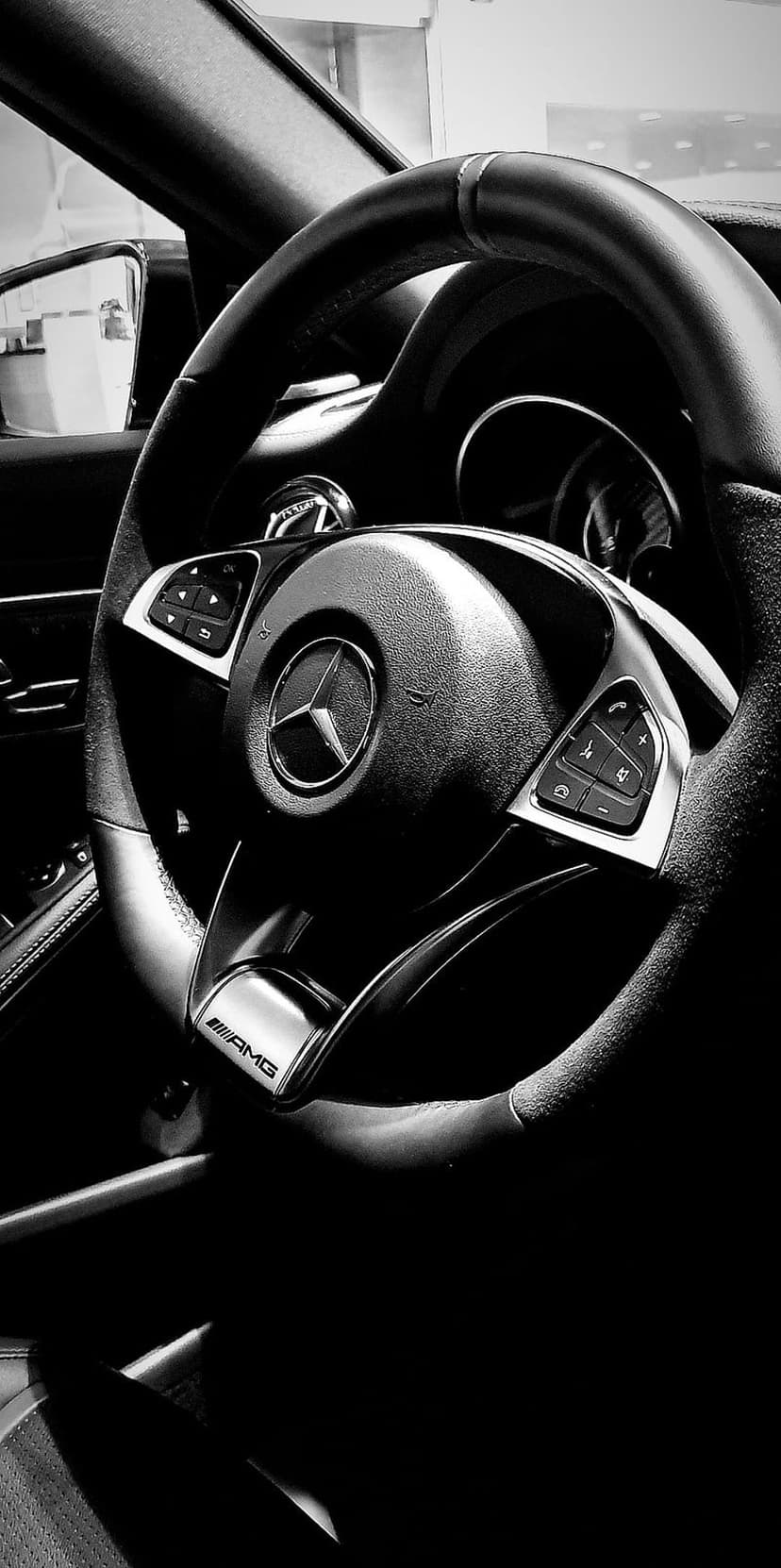 Mercedes-AMG steering wheel with central star logo and leather texture in a black and white close-up view.