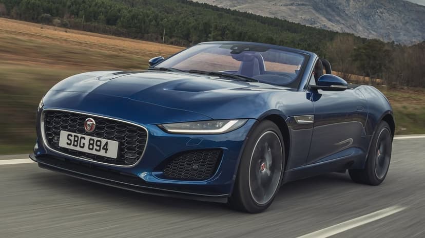 Blue Jaguar F-Type convertible driving on a mountain road with motion blur and green hills in the background.