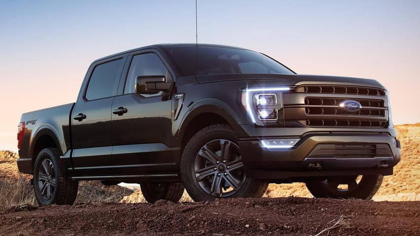 Dark metallic Ford F-150 Lariat pickup truck with glowing LED headlights on a red dirt ridge during a desert sunset.