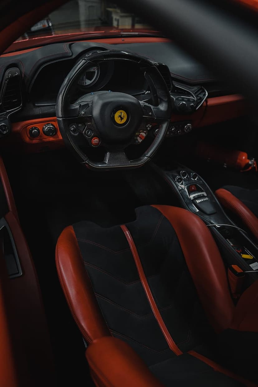 Ferrari red leather racing seats and a steering wheel with a yellow badge inside a luxury vehicle cockpit.
