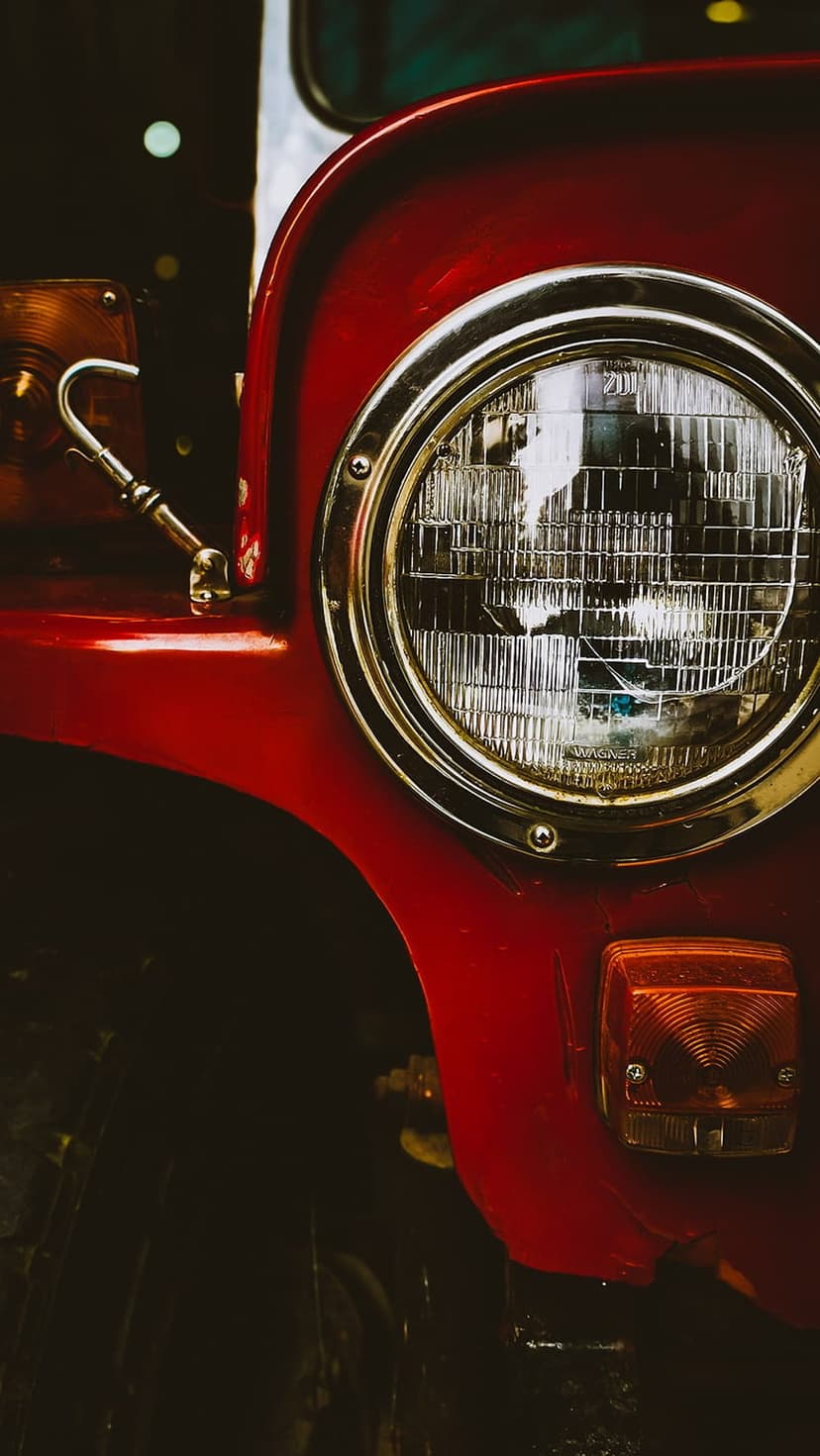 Red vintage jeep headlight with a chrome rim and amber turn signal set against a dark, blurred background.