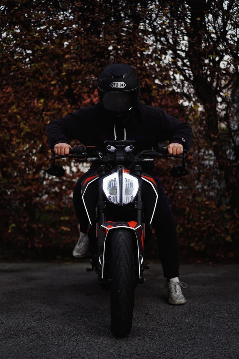 Motorcyclist in a black hoodie and helmet sits on an orange KTM motorcycle with glowing LED lights in autumn.