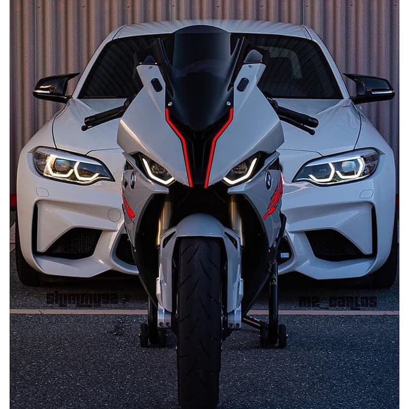 White BMW M2 car and sportbike motorcycle with red accents parked side-by-side against a grey textured wall.