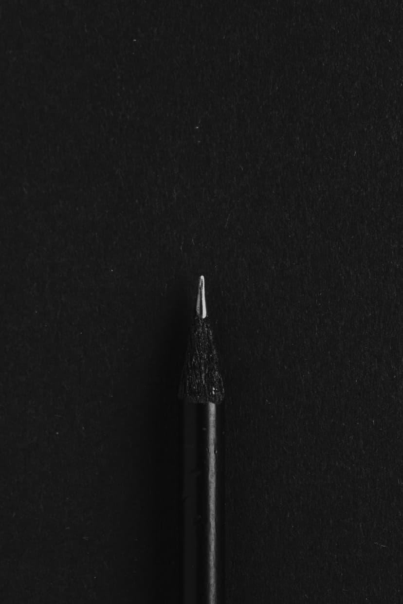 Sharpened graphite pencil tip showing detailed wood grain texture illuminated against a solid black background.