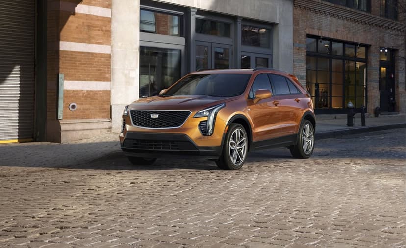 Orange Cadillac SUV parked on a cobblestone street in front of brick buildings during daylight.