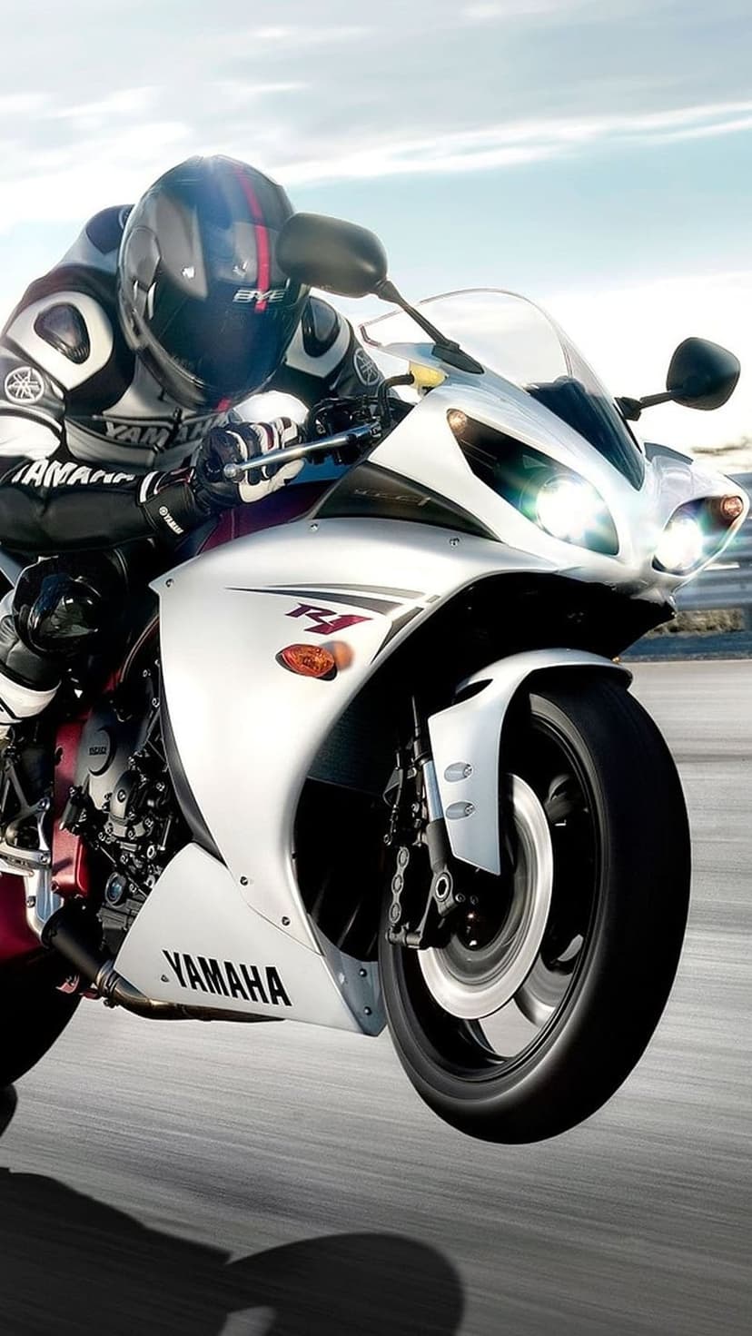 Yamaha R1 rider leaning into a sharp track turn wearing full racing leathers against a clear blue sky backdrop.