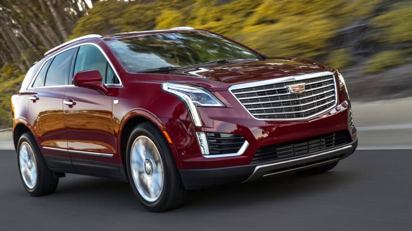Deep red luxury SUV driving fast on a road with blurred forest background and spinning chrome wheels.