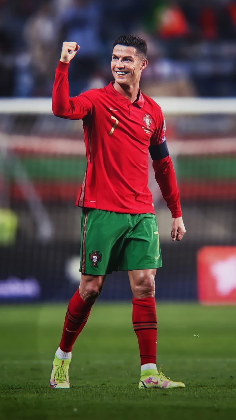 Cristiano Ronaldo raises a fist in triumph wearing a red Portugal jersey on a sunlit professional football pitch.