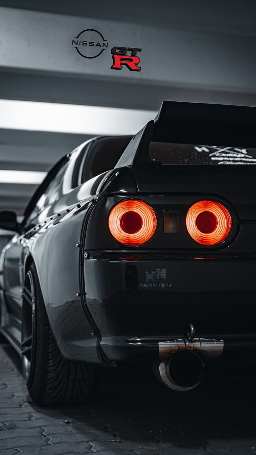 Nissan Skyline R32 GT-R rear circular red tail lights glowing against a sleek black wide-body car frame.