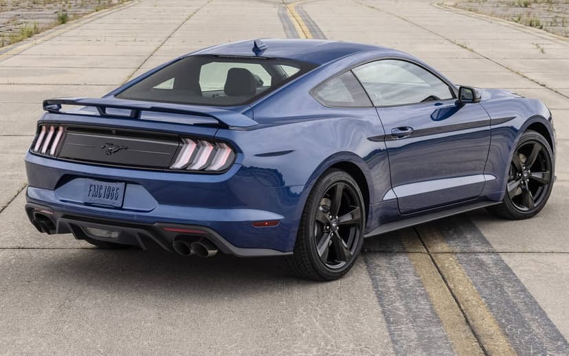 Rear three-quarter view of a blue Ford Mustang with black wheels on a grey asphalt runway with yellow lines.