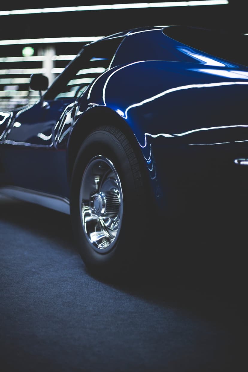 Dark blue Chevrolet Corvette rear fender and chrome spoke wheel reflecting studio lights in a low-angle shot.