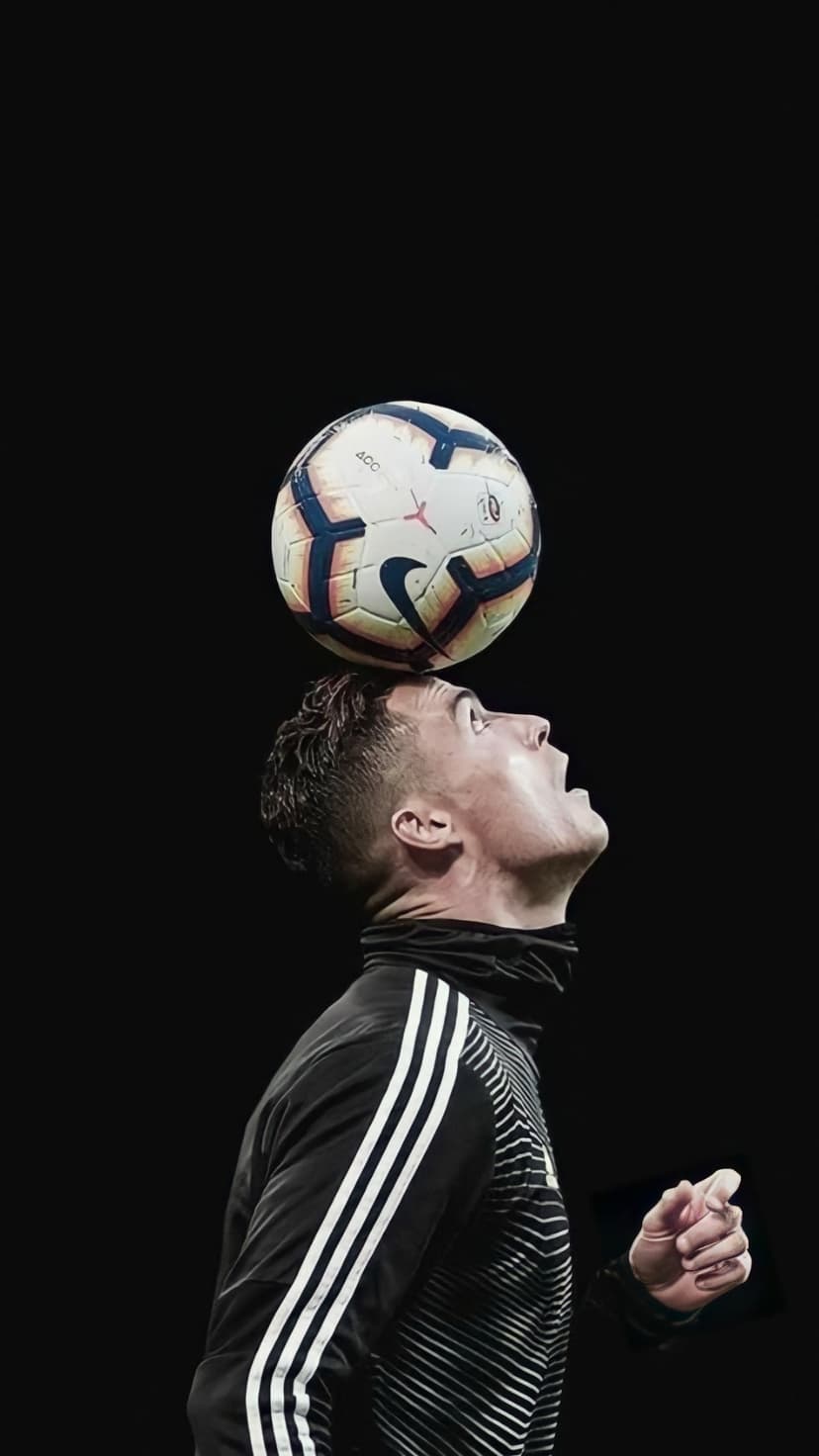 Cristiano Ronaldo balances a soccer ball on his head wearing a black Adidas tracksuit against a dark background.