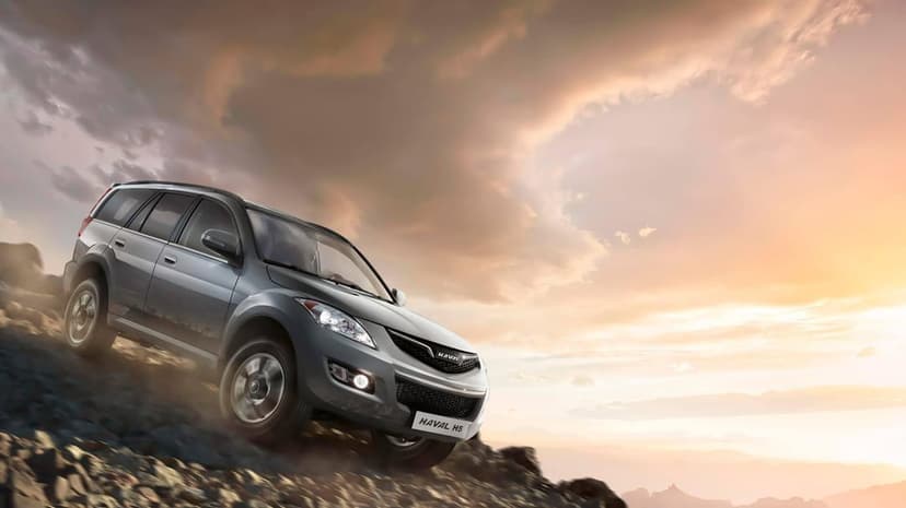 Grey Haval H5 SUV driving down a steep rocky slope under a dramatic orange and purple sunset sky.