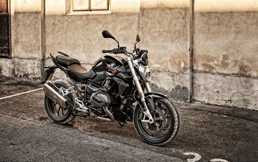Black BMW naked motorcycle parked on asphalt against a weathered stone wall in warm cinematic lighting.