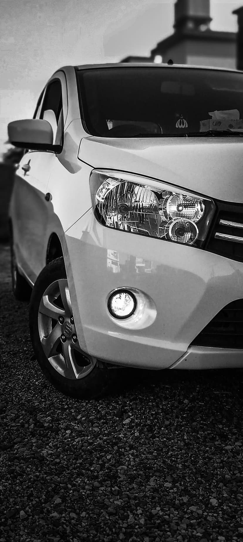 Car headlight and wheel on gravel in black and white with dramatic reflections and sharp mechanical details.