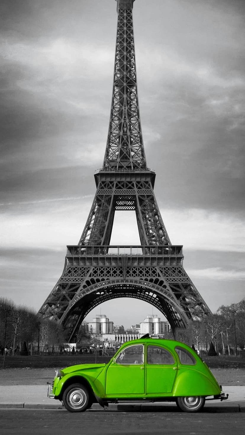 Bright green vintage car parked in front of the black and white Eiffel Tower under a cloudy Parisian sky.