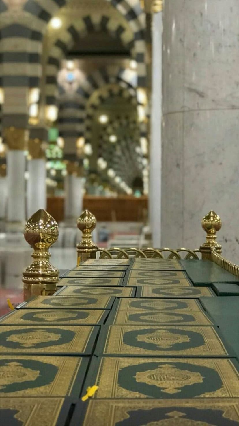 Dark green Quran books with gold patterns sit in rows before striped mosque arches in this spiritual scene.